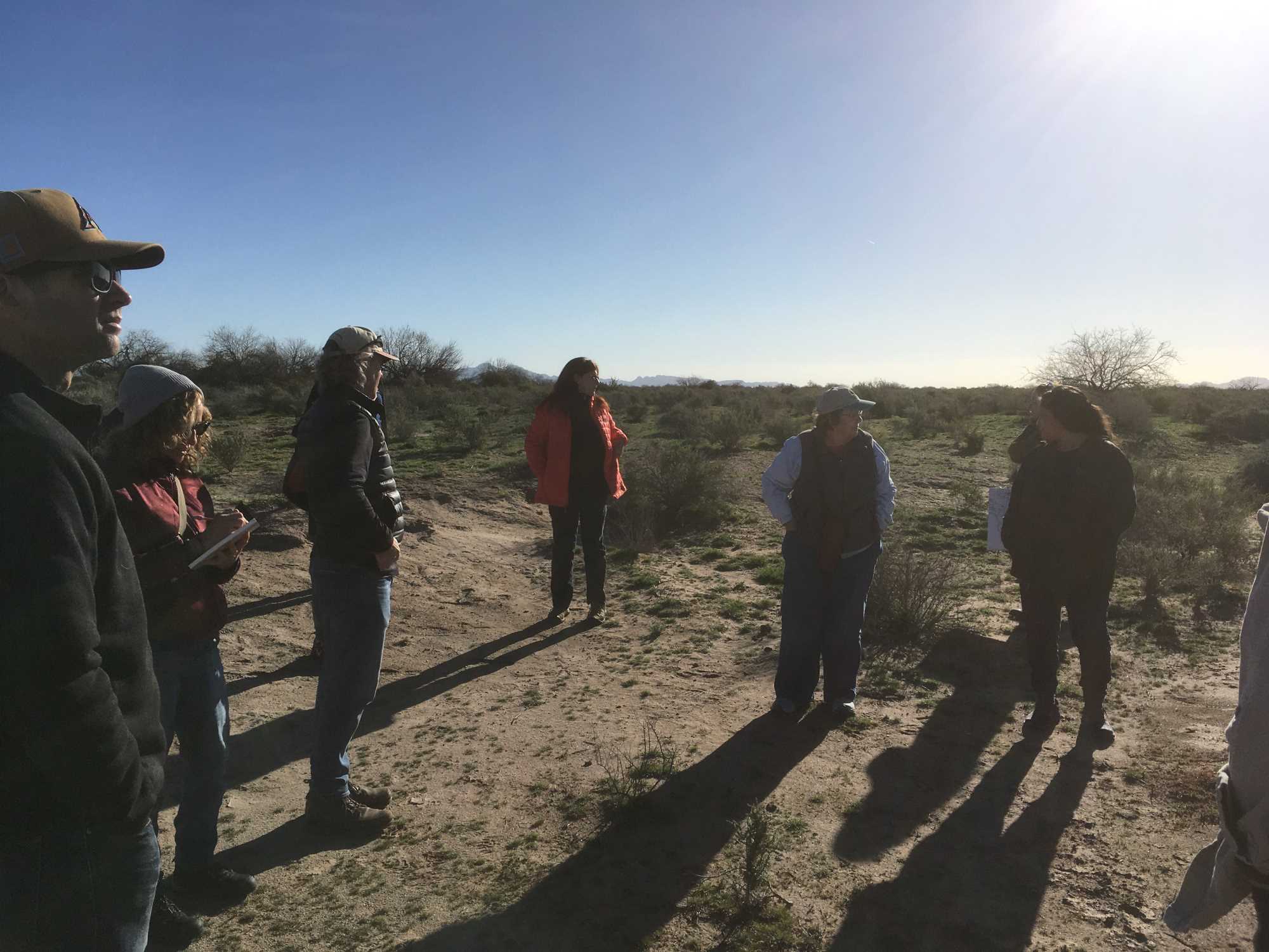 A group of people is visiting an ancestral O'odham site in the early morning light.