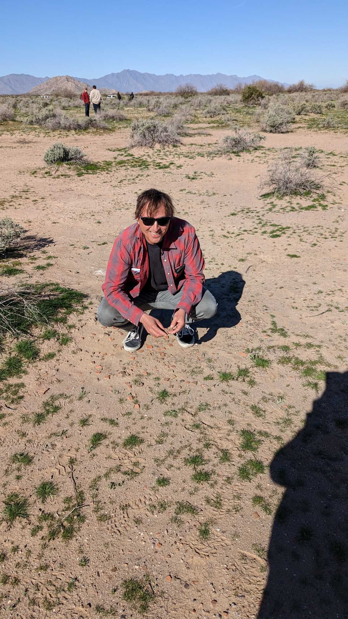 A person is squatting on the ground looking at pottery sherds.