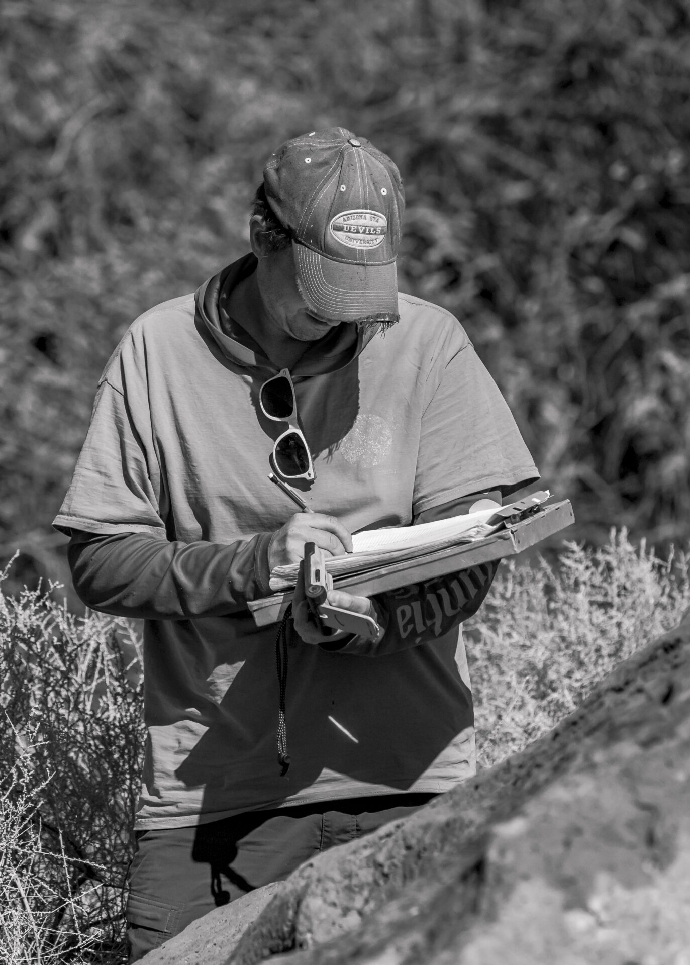 A man in a baseball cap is looking down at a clipboard and is writing.