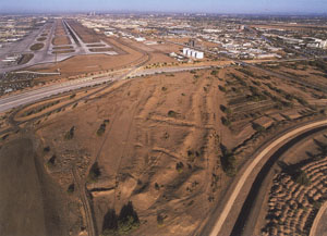Phoenix Basin Hohokam irrigation systems were impressive accomplishments. Two canals are still visible on the ground surface just east of the north runway of Sky Harbor International Airport in Phoenix. These canals appear as subtle linear depressions bounded by linear mounds of soil in the center foreground of this image. Many canals have been documented beneath the airport.