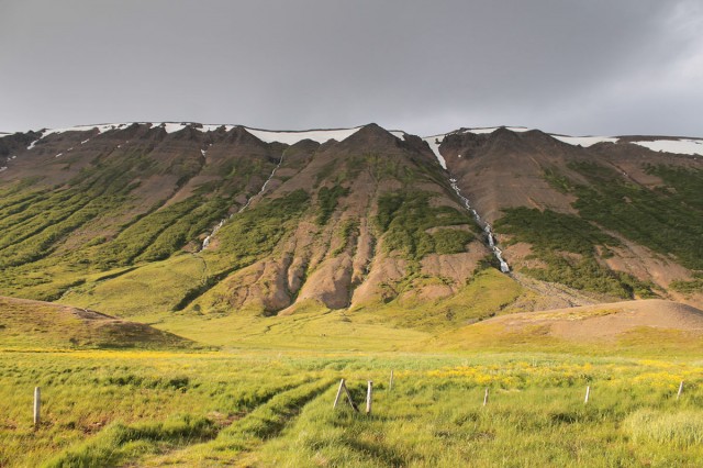 Sunlit escarpment with several snow-fed waterfalls near the ancient farm of Fornholð.