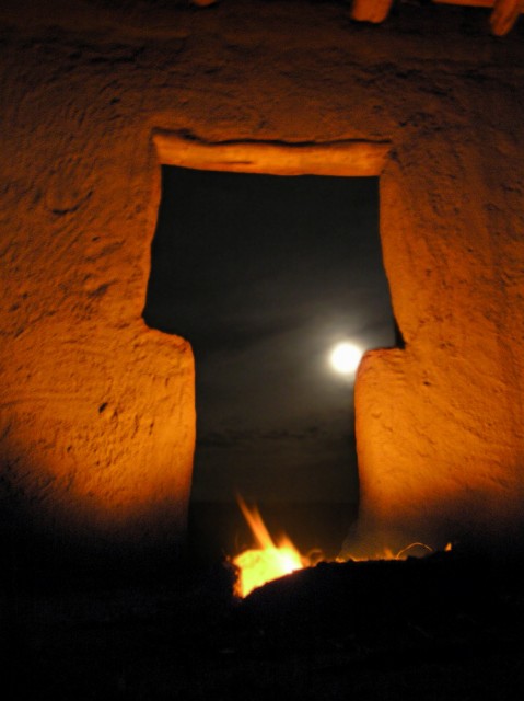 Firelight and moonlight illuminate the entryway at night.