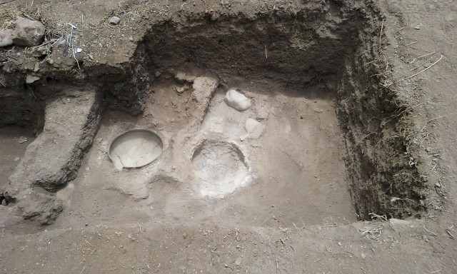 Grinding stations and ceramic vessels in floor pits; remnant of adobe wall on the left.