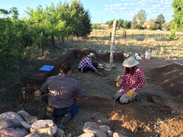 In this image, Karla and Sam are excavating the east trench for the cimiento stones (footer stones). Emily is excavating last year’s mud-mixing pit. The students used digging sticks for these tasks, and the soil they excavated was later used to make mud.