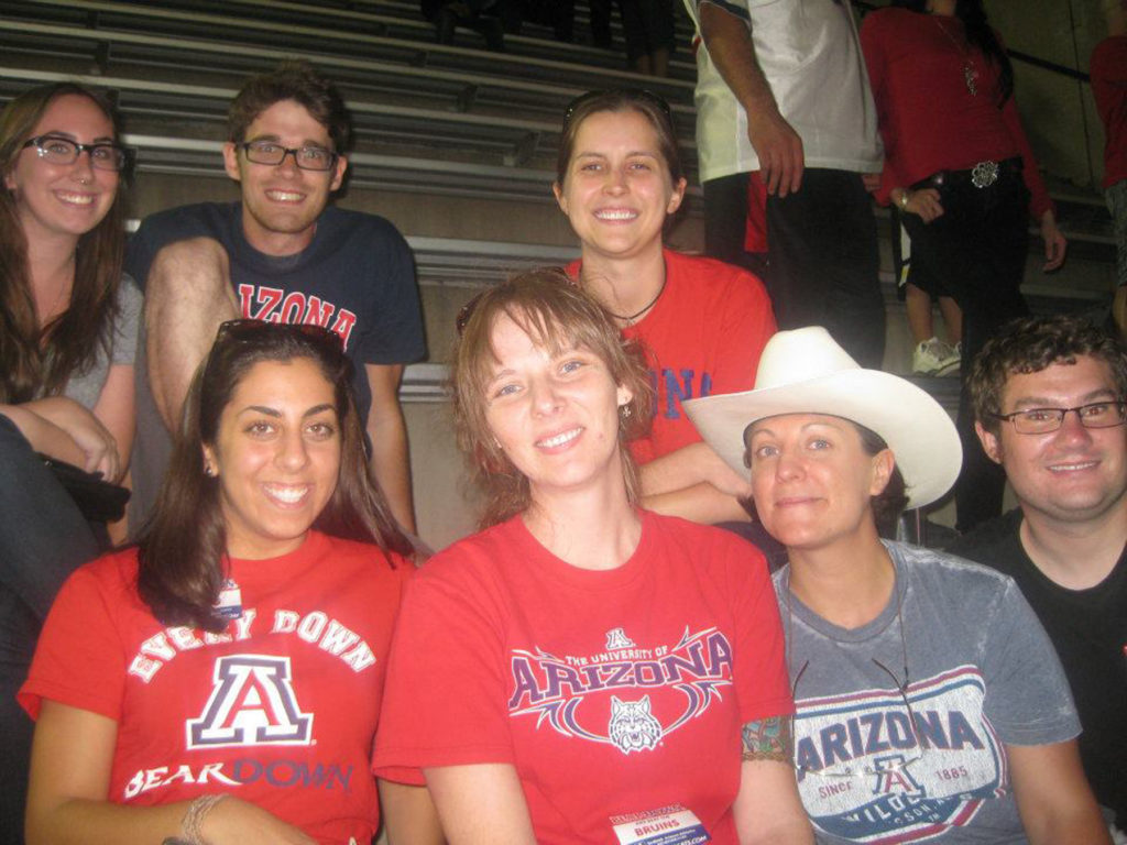 In this photo, I am actively expressing my membership in a group of people who supports the University of Arizona’s sports-ball teams by wearing a tee-shirt with their logo boldly emblazoned on the front.