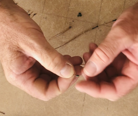 View looking down at two human hands stringing beetle-leg beads onto natural fiber cordage.