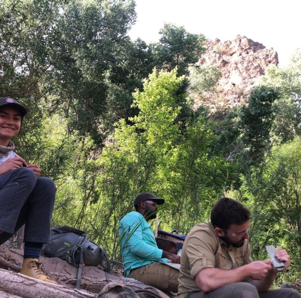 A woman and two men flintknapping on the bank of the San Francisco River in New Mexico.