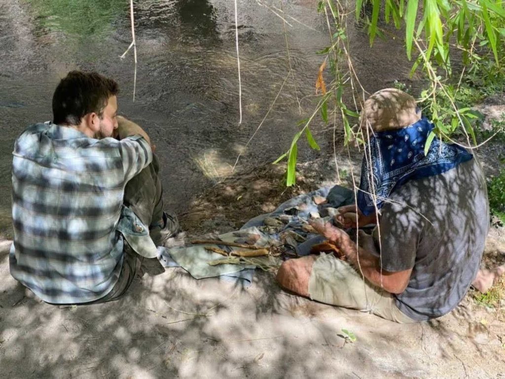 Two men using stone tools to carve wood