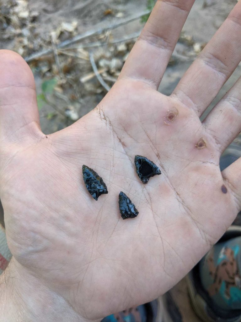 Three small obsidian arrow points held in the palm of the flintknapper