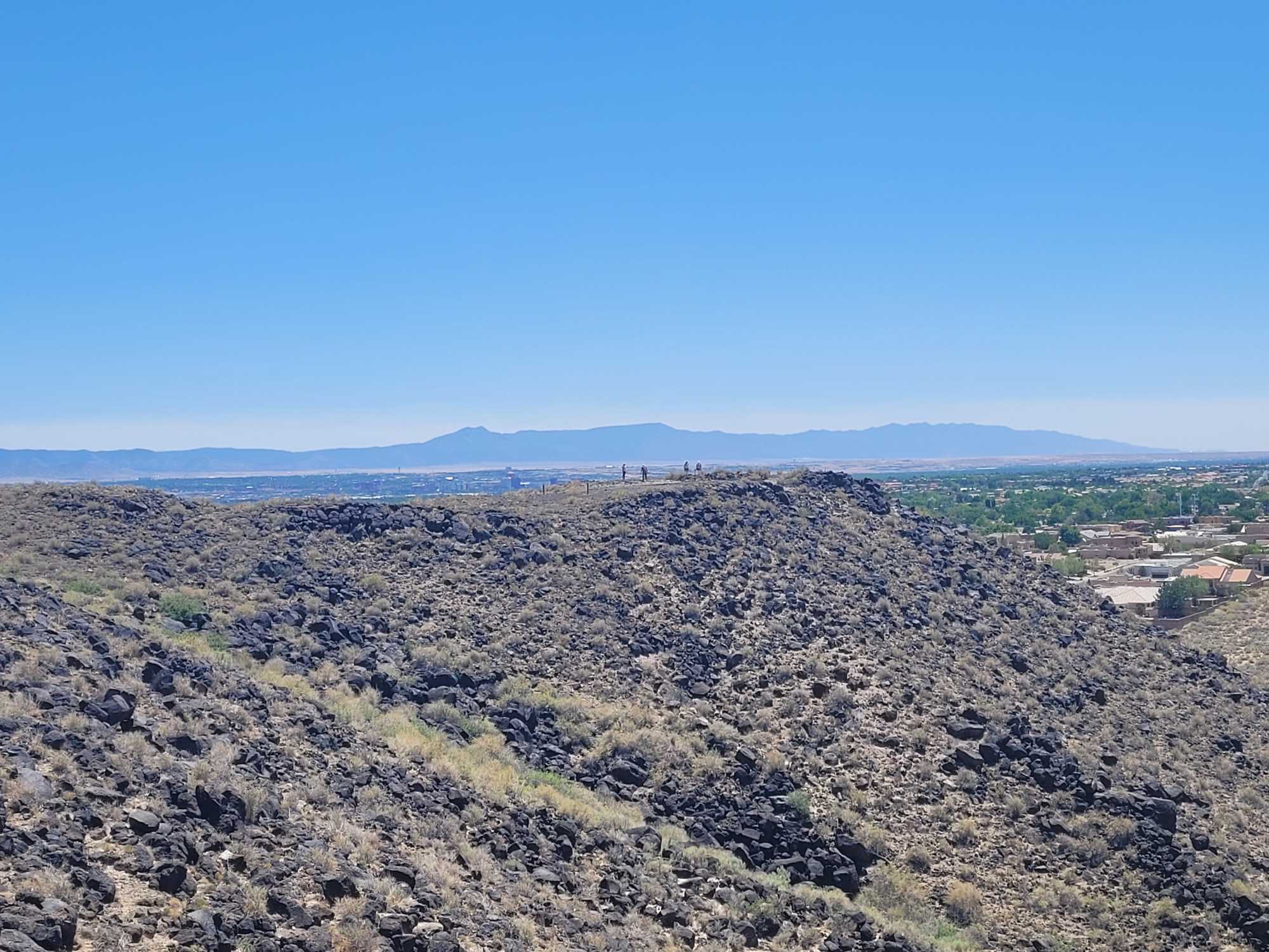 View to east/southwest of escarpment with crew on mesa top and Manzano Mountains in the distance.