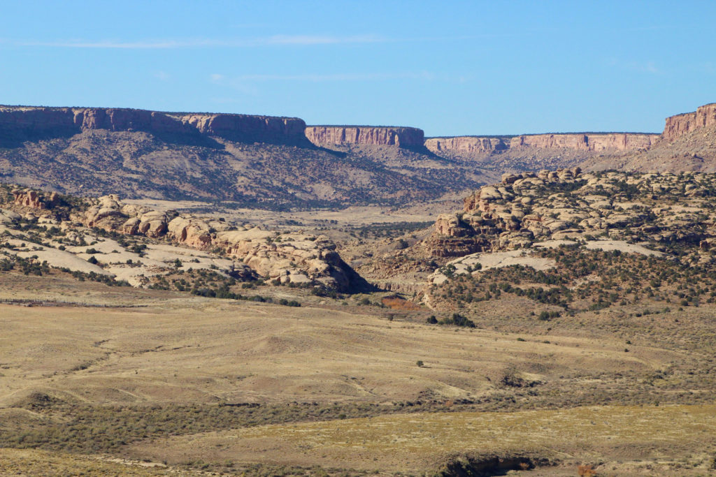 Overview photo of the Morris 40 community, looking west–northwest. Habitations are located just below the line where the sandstone slickrock meets the grasslands. They are found on either side of the deep arroyo that cuts through the New Mexico hogback. Image: Kellam Throgmorton