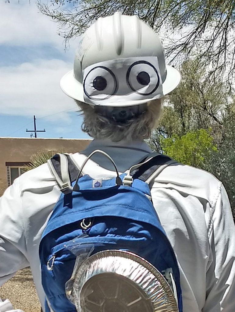 A man pictured from the back wearing a white hard hat with cartton eyes drawn on the back, a backpack, and a pie tin affixed to the backpack. The person in the picture was attacked by a Cooper's Hawk in his yard last week.