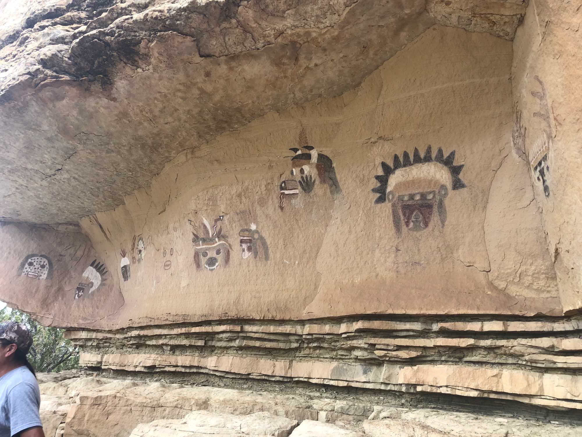 A panel of Zuni pictographs dating to the 1950s and depicting deities and beings embodying animals. This is a stop on an official tour of the Village of Many Kivas, here led by Zuni guide Kenny Bowekaty in June 2022. Image: Totsoni Willeto