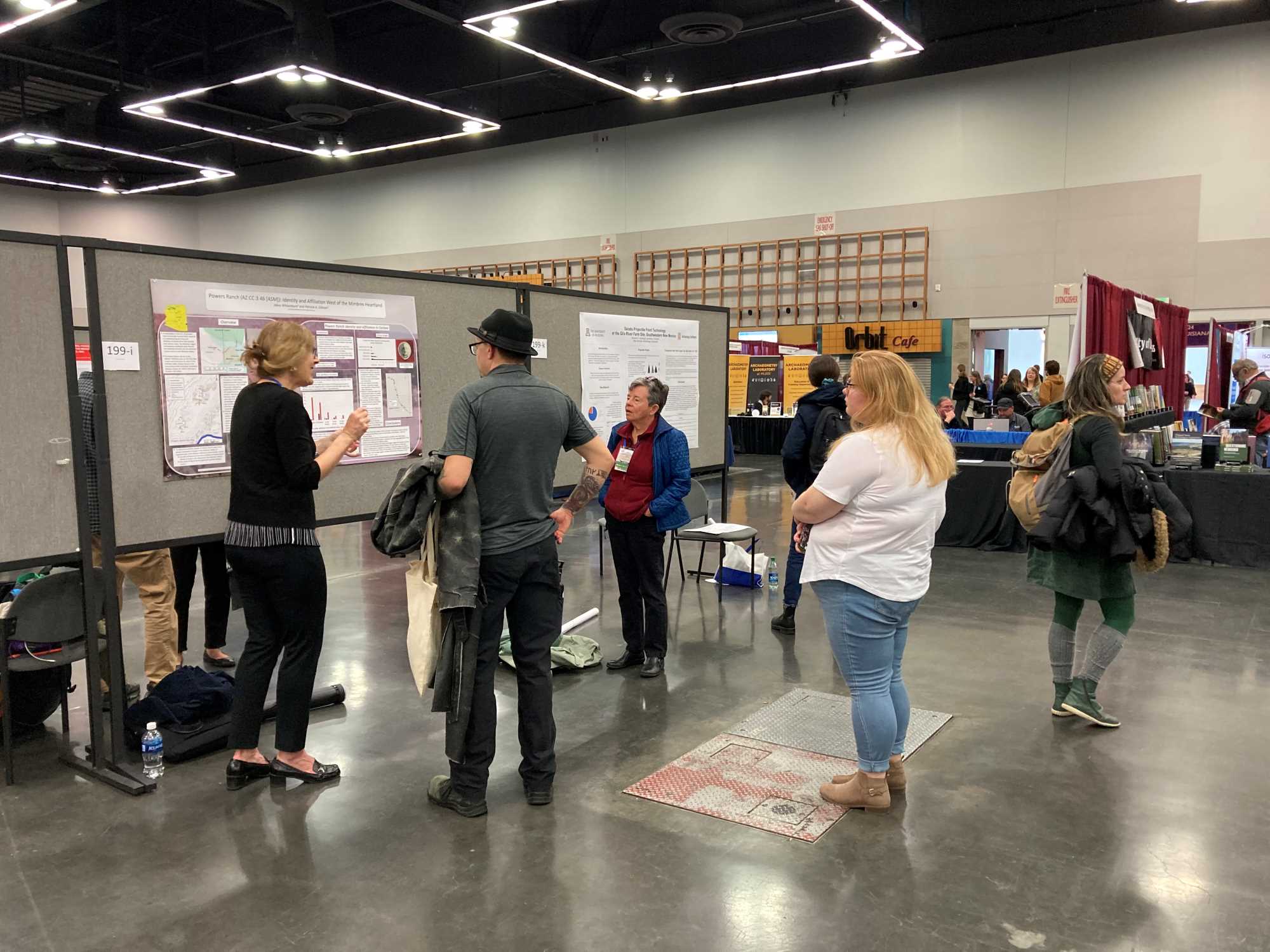 A group of people are standing in an exhibit hall at a conference center. They are looking at research posters tacked onto moveable walls.