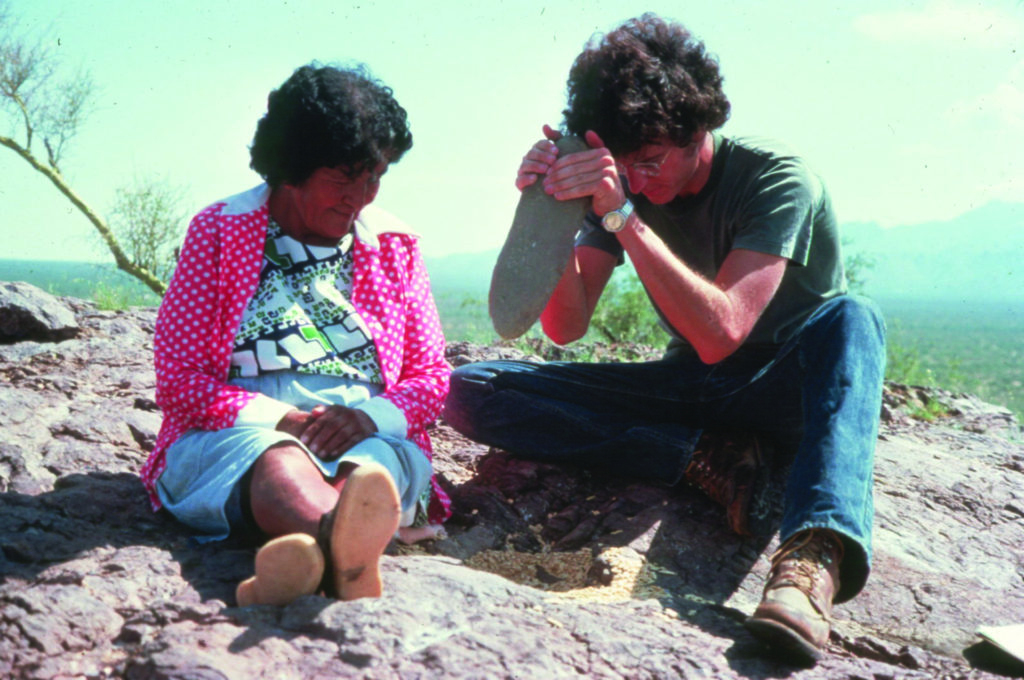 As part of his dissertation research in the mid-1970s, Archaeology Southwest founder and CEO Bill Doelle (right) practiced mesquite processing with a stone pestle and bedrock mortar under the tutelage of Juanita Ahill (left), a member of the Tohono O’odham Nation. Image: Helga Teiwes