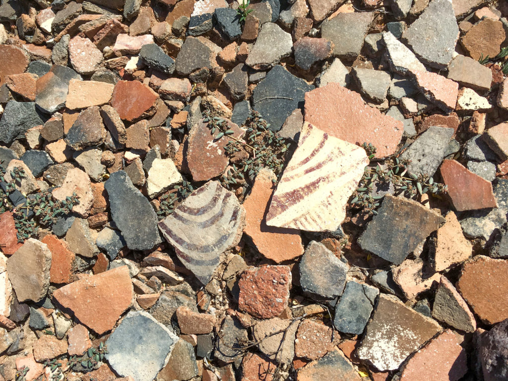 Decorated pottery sherds with a red-painted design amidst a pile of plain pottery.